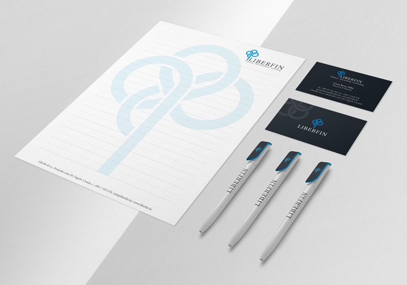 The picture shows (on a white background) a white letterhead with an applied Liberfin logo icon in blue, two black business cards with a Liberfin logo design on them, and three ballpoint pens in dark blue and white with the logo.