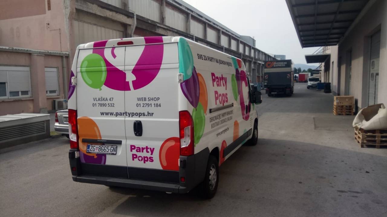 Vehicle wrap design for the company Party Pops from Zagreb, Croatia. The picture shows a colorfully painted van. In the center is the Party pops company logo, a magenta circle with a white heart-shaped balloon inside. The logo is surrounded by other balloons in various colors and on the side you can see the text Party Pops with their slogan and basic information.