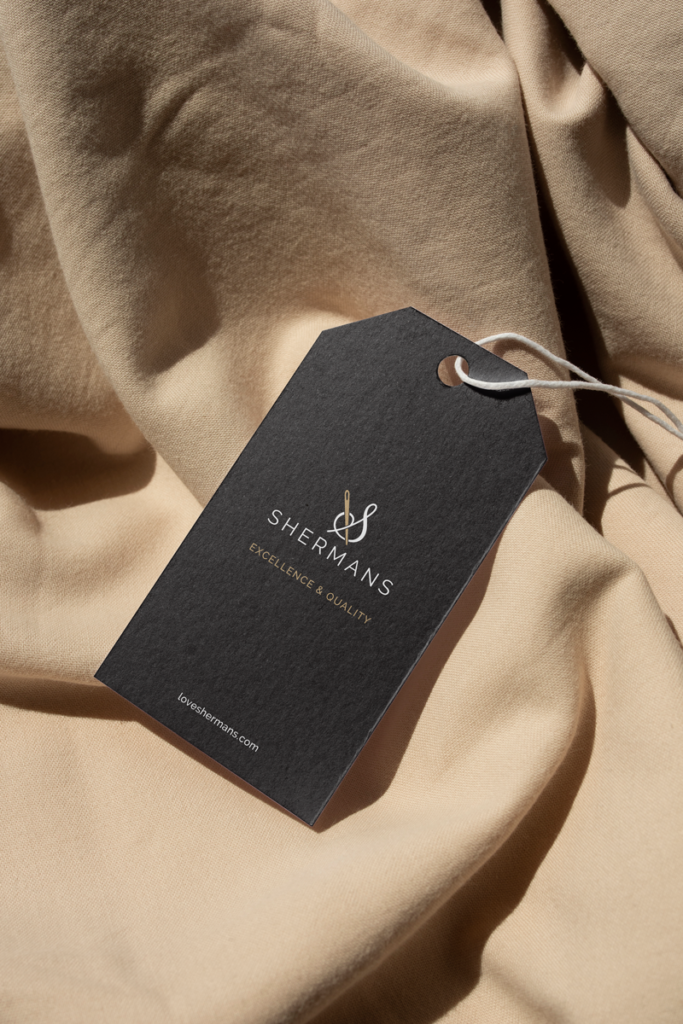 Label design for fashion brand Shermans. The picture shows a black clothing label on a beige fabric.