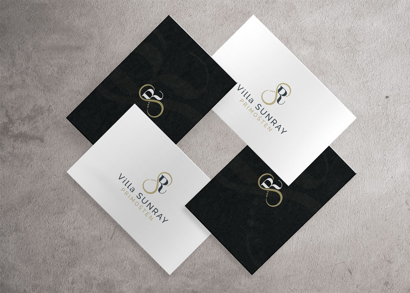 Business card design for Villa Sunray apartments. The picture shows 4 business cards stacked in a circle on a concrete base. Two business cards are black, two are white. They all have the design of the Villa Sunray Apartments logo.