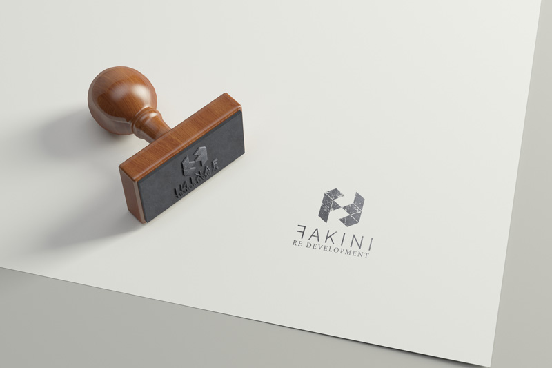 In the picture we see a white sheet of paper with the Fakini logo printed in black ink. A wooden stamp is placed on the paper.
