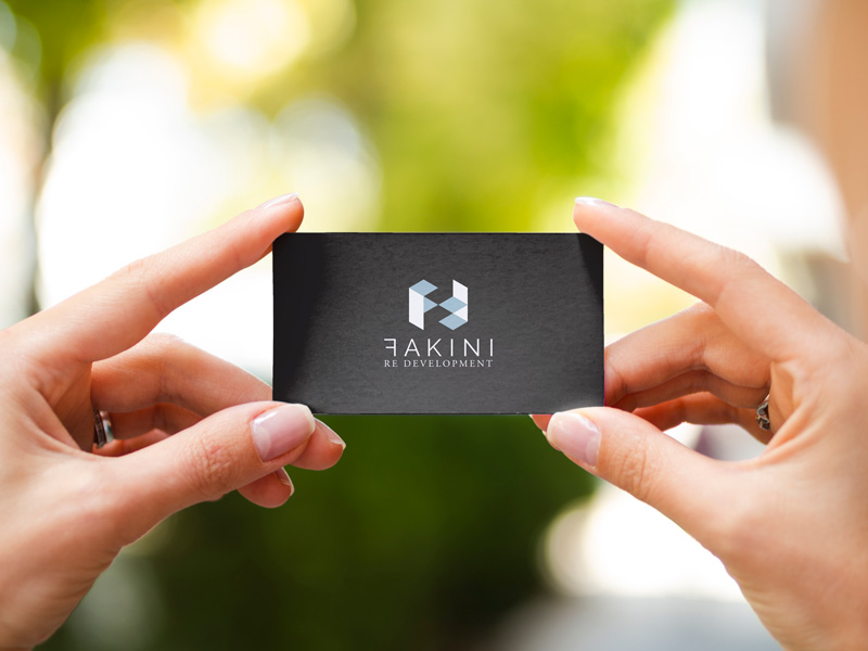 In the picture, we see women's hands holding a black business card with an applied Fakini logo design. In the background we see blurred nature.