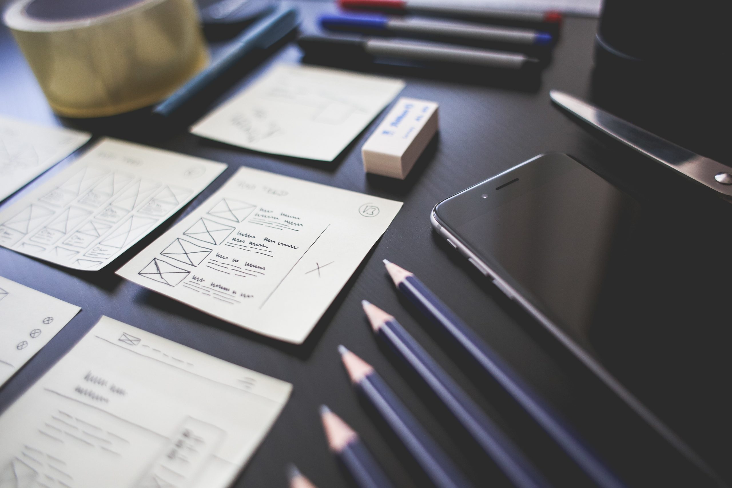 Blog o UX i UI dizajnu: crni radni stol prepun bilježnica i olovki sa dizajnom UX u procesu izrade