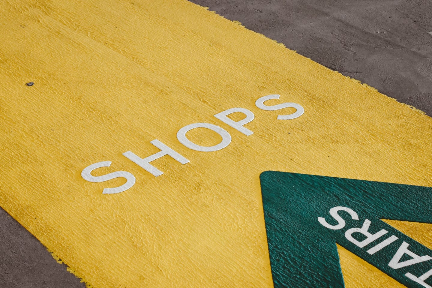 Oznaka za usmjeravanje na podu: bijeli natpis „Shops” na žutoj traci i zelena strelica