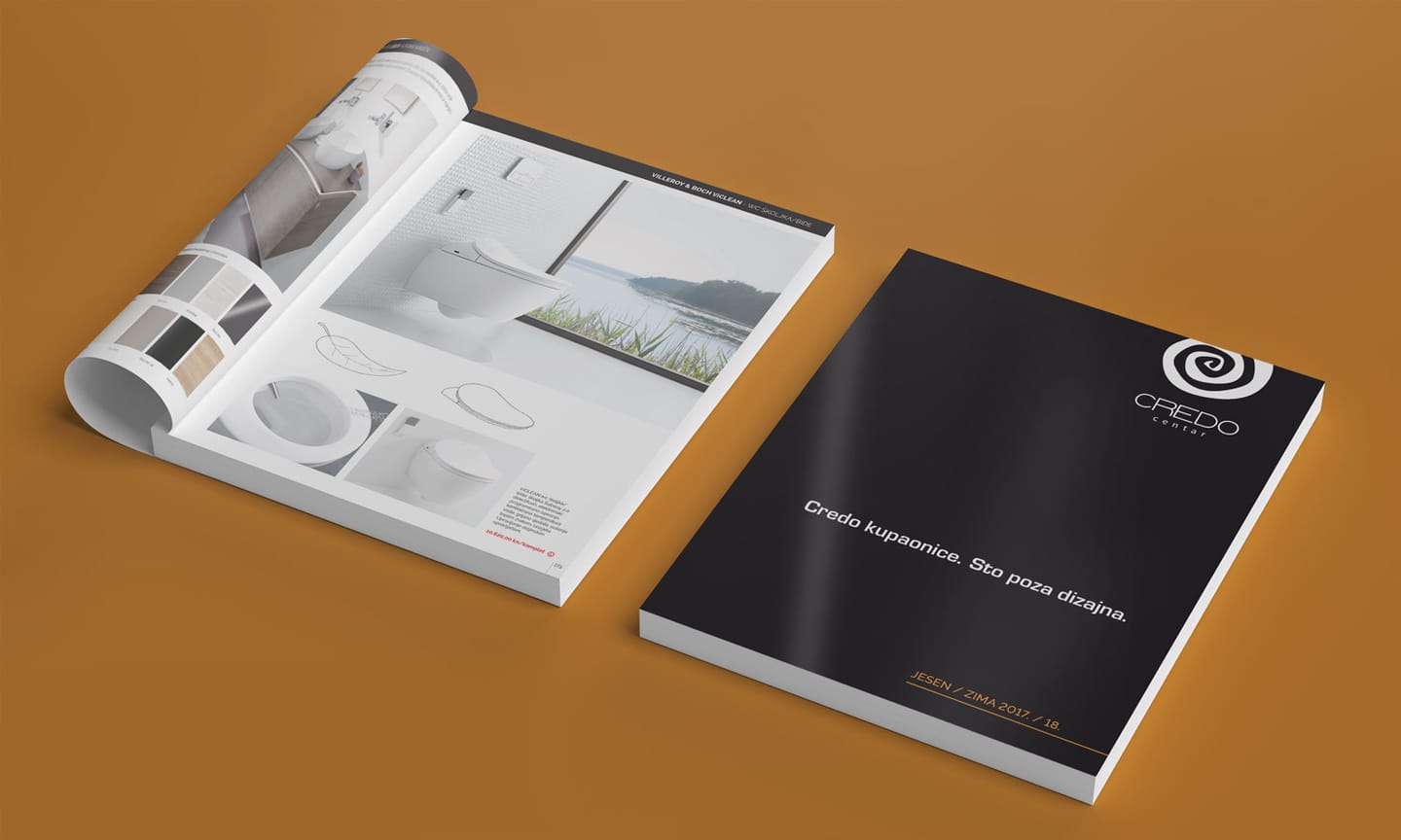 Credo centar catalogues on a bright orange background: one closed, showing the black and white cover, and one open at a bathroom page