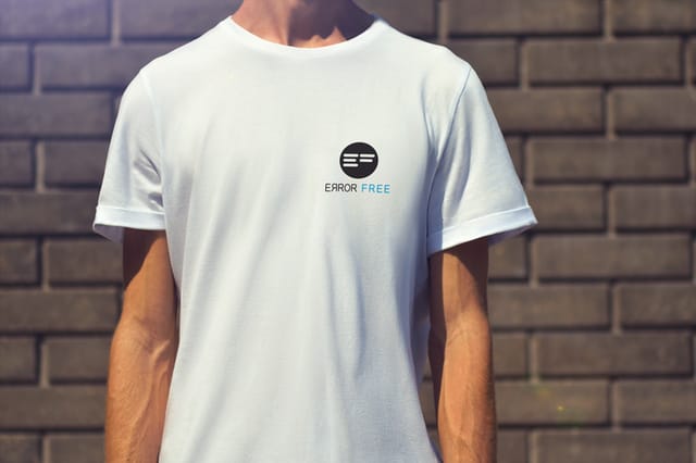 White promotional T-shirt with the Error Free logo on the chest, worn by a model in front of a brick wall