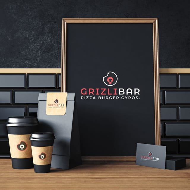 Vizualni identitet Grizli bara: crni plakat s logotipom u drvenom okviru, šalice za kavu, papirnata vrećica i posjetnice na drvenom stolu ispred tamnog zida