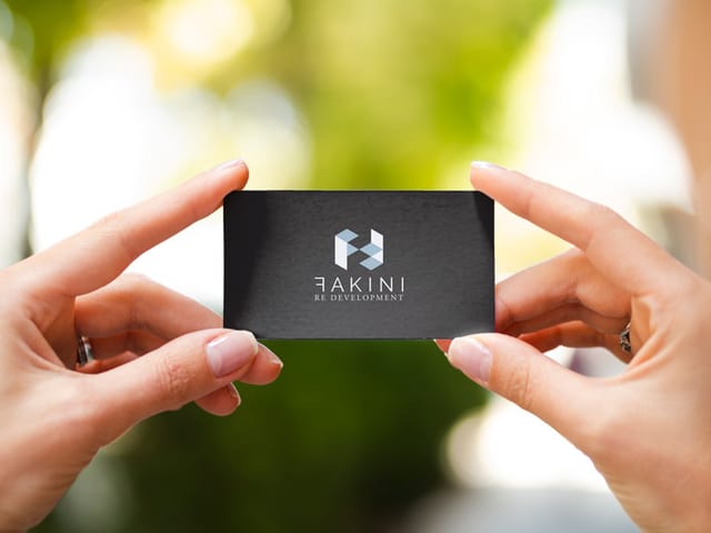 A woman’s hands holding a black business card with the Fakini logo, against a blurred natural background