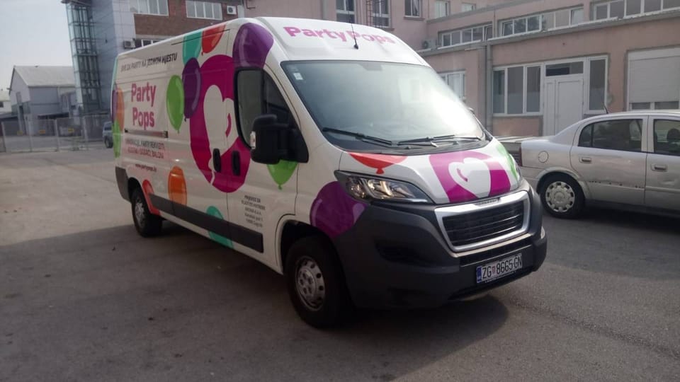 Party Pops van wrap, seen from the front: a magenta circle with a white heart-shaped balloon, colourful balloons and the Party Pops name with the slogan and contact details