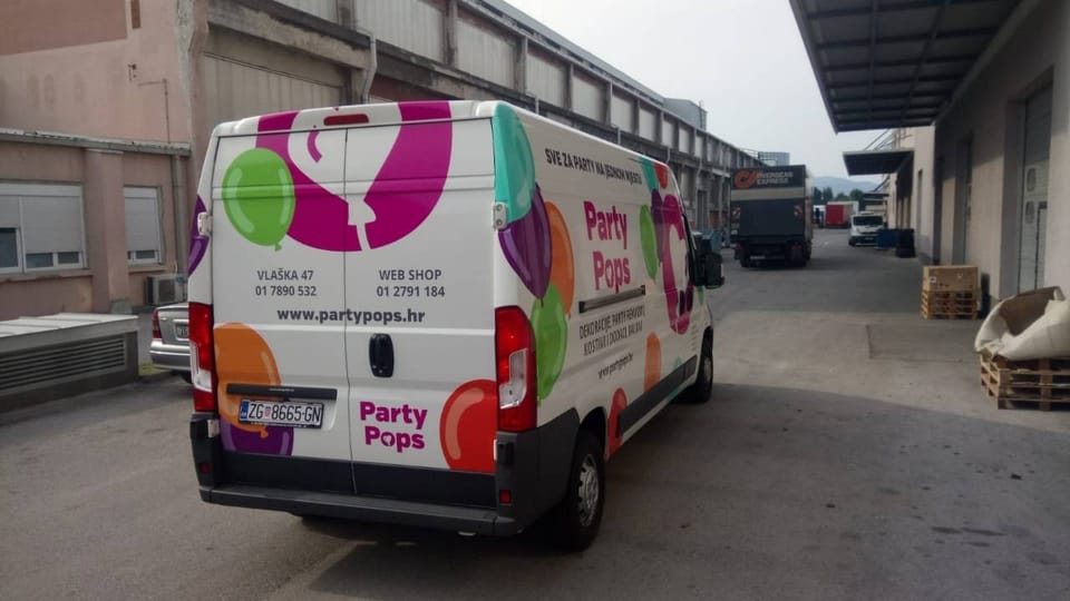 Party Pops van wrap, seen from behind: a magenta circle with a white heart-shaped balloon, colourful balloons and the Party Pops name with the slogan and contact details